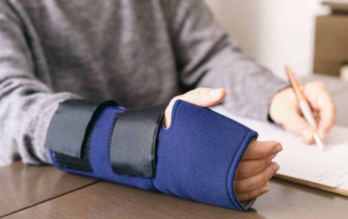 Close-up of a person's arm in a wrist brace while writing, representing workplace injury recovery and rehabilitation.