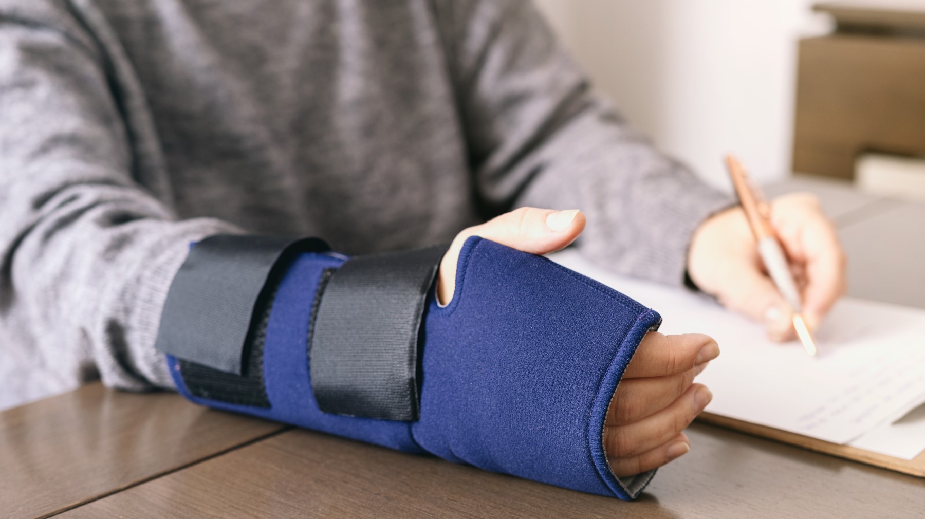 Close-up of a person's arm in a wrist brace while writing, representing workplace injury recovery and rehabilitation.