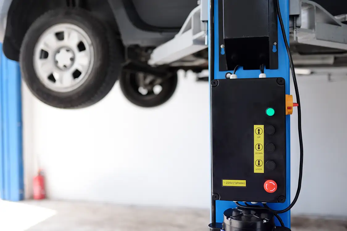 Control panel for a hydraulic car lift in an auto repair shop with a vehicle raised in the background.